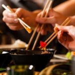 Young people eating in a Thai restaurant, they eating with chopsticks, close-up on hands and food