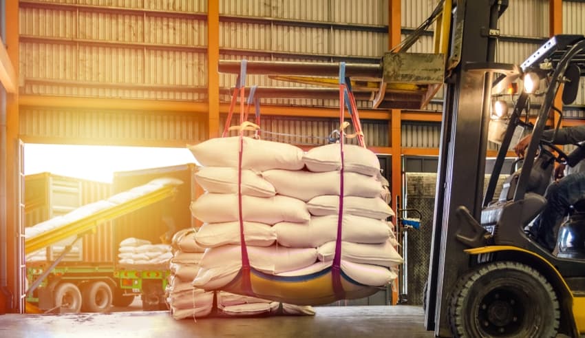 Forklift handling white sugar bags for stuffing into containers outside a warehouse