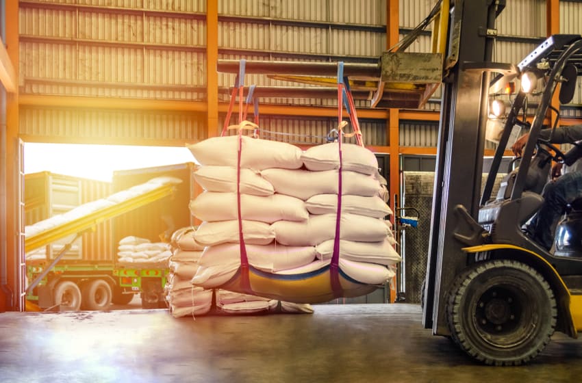 Forklift handling white sugar bags for stuffing into containers outside a warehouse
