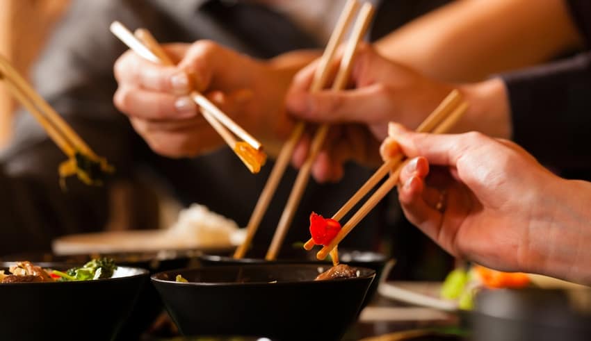 Young people eating in a Thai restaurant, they eating with chopsticks, close-up on hands and food